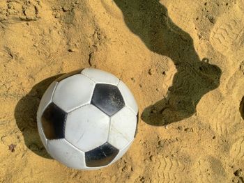 Shadow of person leg with soccer ball on sand
