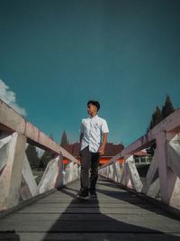 Full length of young man standing on bridge against sky