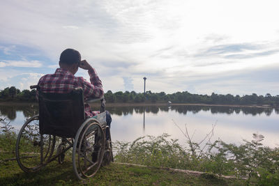 Man sitting by lake against sky