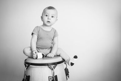 Portrait of baby boy sitting on drum against wall