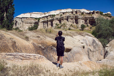 Male hiker with backpack in sneakers is in the mountains and the rocks in uchisar