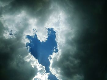 Low angle view of sunlight streaming through clouds