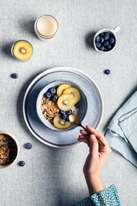 Top view of crop anonymous female with breakfast with bowl with granola and blueberries and kiwi slices