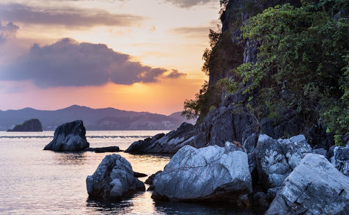 Rocks in sea against sky during sunset