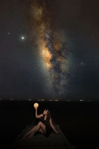 Man sitting by rock against sky at night