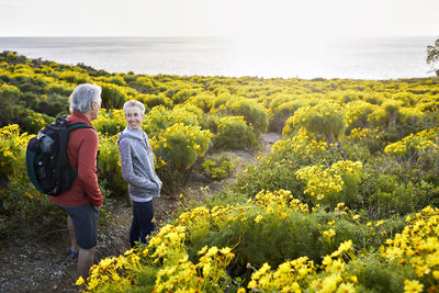 High angle view of senior couple talking while standing on trail by flowers plants against bright sky