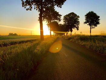 Road amidst field against sky during sunset