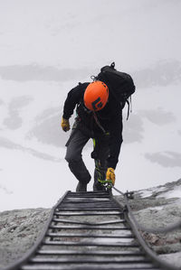 High angle view of male hiker moving up on ladder amidst mountain during winter
