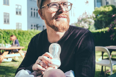 Mid adult man looking away while feeding milk from bottle to baby boy at park