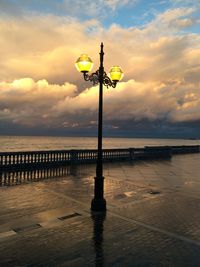 Street light by sea against sky during sunset