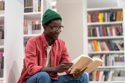 Interested african american student guy reading book in university library, studying for exam.