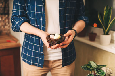 Easter day. adult man holding basket with eggs on wooden background. stay in a kitchen with nest.