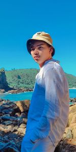 Portrait of young man standing at beach against clear blue sky