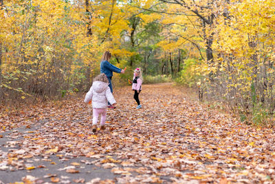 Full length of mother playing with daughters in forest during autumn