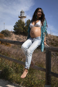 Portrait of beautiful pregnant woman against sky with a lighthouse behind 
