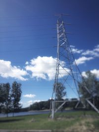 Low angle view of electricity pylon on field against cloudy sky