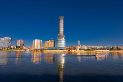 Buildings by river against clear blue sky