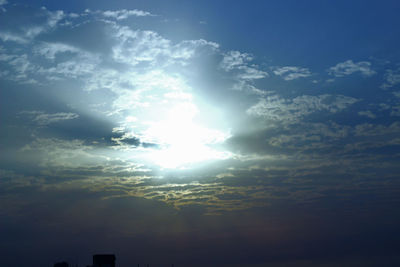 Low angle view of sun shining through clouds