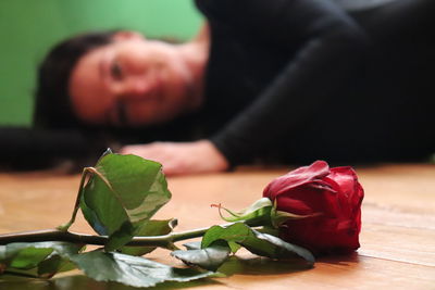Close-up of red rose with woman lying down in background on floor