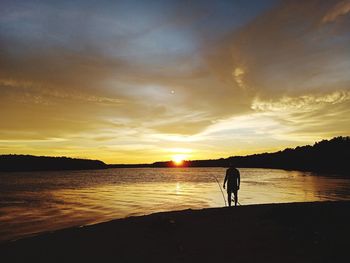 Silhouette man standing by lake against sky during sunset