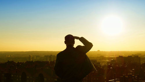Rear view of man shielding eyes against sky during sunset
