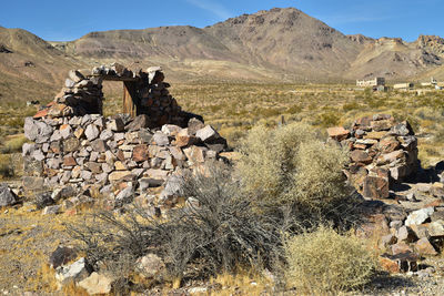 Deteriorating walls abandoned stone house in mojave desert with one window frame with mountain view