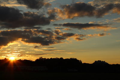 Silhouette trees on field against orange sky