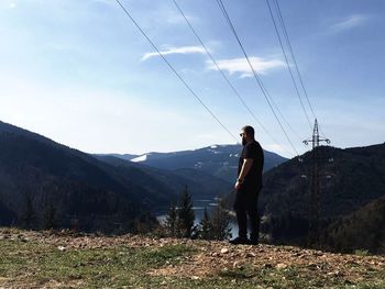 Man standing on peak while looking at mountains against sky