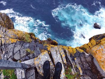 Person in black shoes standing on rocky cliff by sea