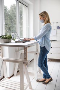 Side view of businesswoman wearing mask using laptop at home