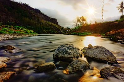 Rocks by river against sky