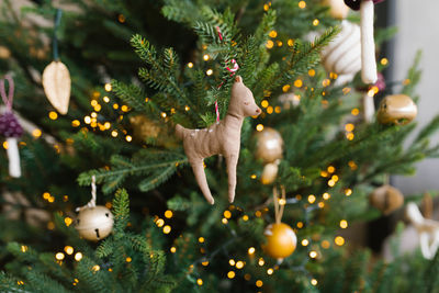 Toy hand made fawn hanging on the christmas tree with lights. holiday card