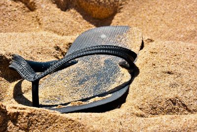 Close-up of messy flip flop in sand on beach