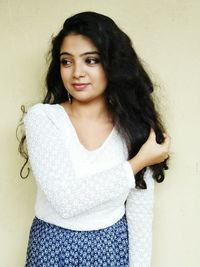 Portrait of smiling young woman standing against wall