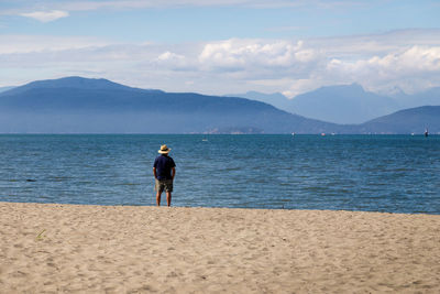 Rear view of man standing on beach against sky