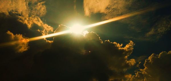 Low angle view of sunlight streaming through clouds during sunset