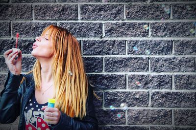 Woman blowing bubbles against brick wall