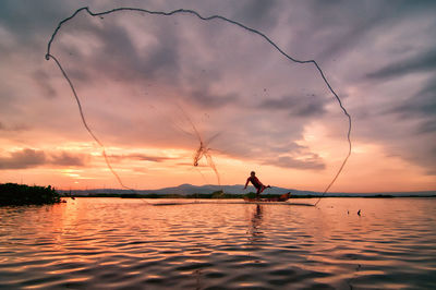 Silhouette man fishing in sea against sky during sunset