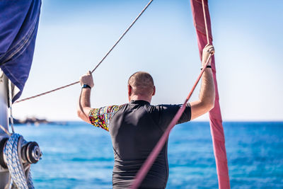 Rear view of man standing on sailboat against sea