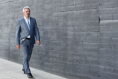 Mature businessman walking by gray wall