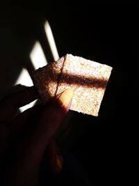 Close-up of hand holding ice cream cone against black background