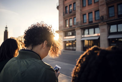 Teenage girl using phone while standing with friends by street in city