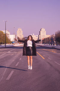 Full length portrait of woman in mid air on street against clear sky