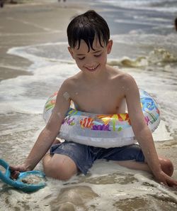 Full length of shirtless boy sitting on sand at beach