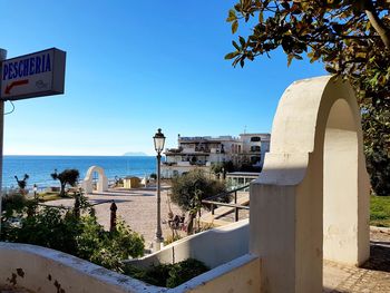 Buildings by sea against clear blue sky