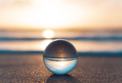 Close-up of crystal ball on beach against sky during sunset