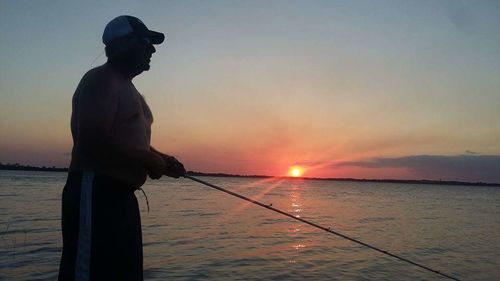 Man fishing in sea at sunset