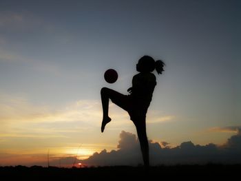 Silhouette woman playing with ball against sky during sunset