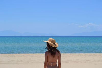 Rear view of sensuous woman wearing hat against sea at beach