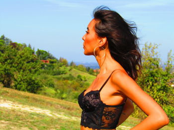 Side view of young woman standing against trees